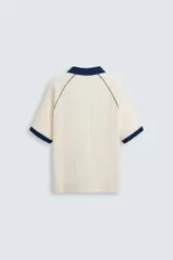 Polo color crema con cuello solapa azul marino, mangas cortas con ribete azul marino, bordado de texto en el pecho y bordado de logo en el abdomen.