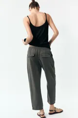 Pantalón gris oscuro de tiro alto con cintura elástica, bolsillos delanteros y falsos bolsillos con solapa en la espalda. Cierre frontal con cremallera y botón.
