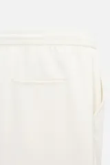 Bermuda color beige de corte recto, con cintura elástica ajustable con cordón, detalle de pliegues frontales, bolsillos laterales y bolsillos de vivo en la espalda.