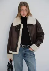 Chaqueta marrón de cuero vegano con forro de sherpa color crema. Presenta solapas con hebillas, cuello italiano, cierre de cremallera y mangas con puños.