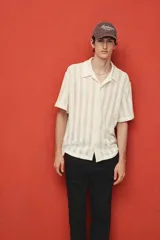 Camisa de manga corta color crema, confeccionada en tejido de punto jacquard con textura calada. Tiene cuello inglés, tapeta clásica con botones y bajo recto.