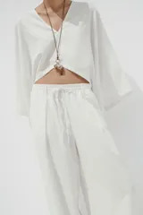Pantalón blanco de lino, de corte ancho, tiro medio, con trabillas y cintura elástica ajustable con cordones.