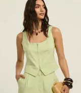 Chaleco corset de sastrería color verde claro, con escote en U, cierre frontal con cremallera, bolsillos falsos y bajo en V.