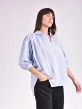 Camisa celeste con cuello mao, corte holgado, mangas 3/4 abullonadas con puños elásticos y cierre frontal con botones.