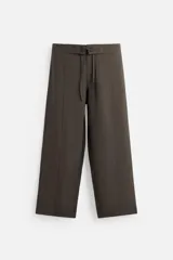 Pantalón marrón oscuro de corte amplio, con cintura ajustable con cordón, bolsillos plastrón delanteros y traseros, detalle de costuras frontales y cierre frontal con cremallera y gancho metálico oculto.