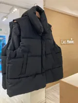 Chaleco puffer negro acolchado, con corte sin mangas y cierre frontal.