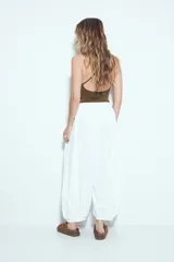 Pantalón blanco de tiro bajo, estilo baggy o aladín, con silueta amplia y fluida, cintura elastizada y puños ajustados en los tobillos.