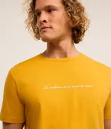 Remera de hombre color mostaza, de corte comfort, con cuello redondo y manga corta. Estampa frontal con la frase "La confiance est le secret du succès" en color blanco.
