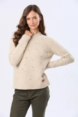 Buzo tejido de abrigo color beige, con cuello redondo y mangas largas. Presenta un delicado diseño bordado en el frente con pequeños motivos en tonos pastel.