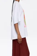 Camiseta color crema de algodón con estampado de un cuadro con borde celeste, con una mano sosteniendo una flor y el texto "Bimba y Lola".