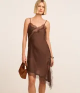 Vestido corto de satén color marrón oscuro con breteles finos y escote en V. Presenta detalles de encaje en el busto y un ruedo asimétrico con terminación en encaje.