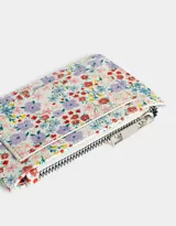 Tarjetero de cuerina con estampado floral multicolor, cierre superior con cremallera y bolsillo frontal abierto.