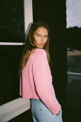 Chaqueta de punto rosa con cuello redondo y manga larga. Tiene bolsillos delanteros y cierre frontal con botones celestes.