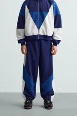 Pantalón deportivo azul marino con paneles laterales blancos y detalles en azul eléctrico. Corte relaxed fit, cintura elástica ajustable con cordón, bolsillos frontales ocultos y puños elásticos.