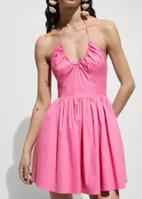 Vestido corto rosado con escote halter, espalda descubierta, falda acampanada y cierre lateral con cremallera.