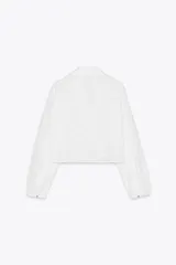 Camisa corta blanca con bordados perforados, cuello solapa, escote pico y manga larga abullonada.