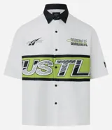 Camisa blanca oversized de tricolina con cuello negro contrastante, mangas cortas y estampado con la palabra "Hustle" en verde y negro.