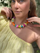 Collar corto con cuentas de resina y cerámica de colores naranja, rosa, verde, celeste y beige. Tiene tiento sintético con cierre ajustable.