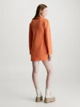 Vestido corto naranja de punto de algodón elástico con textura de canalé. Tiene cuello polo en V, mangas largas acampanadas e insignia con el monograma de Calvin Klein en el pecho.