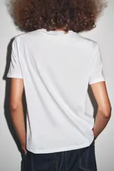 Camiseta blanca de corte recto y manga corta, con estampado frontal de una fotografía en blanco y negro y texto "Amsterdam 74".
