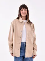 Camisa color marrón claro, de corte recto, con cuello clásico, cierre frontal con botones a presión, bolsillo de parche en el pecho y mangas largas.