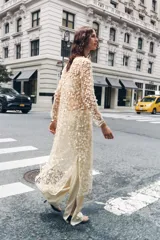 Vestido largo color crema con lentejuelas, de cuello redondo y manga larga. Tiene aberturas laterales en el bajo y cierre con abertura y botón en la espalda.