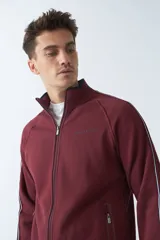 Campera de felpa color bordó con cierre frontal, cuello elevado, bolsillos laterales con cierre y logo estampado en el pecho.