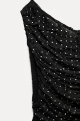 Top negro de encaje con strass, escote asimétrico y hombro descubierto.