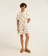 Vestido corto evasé color crema con estampado de soles negros, cuello redondo con lazo, mangas cortas y bajo con volantes.