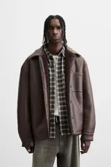 Sobrecamisa marrón de efecto piel con interior de borreguillo combinado a tono, de corte relaxed fit, cuello solapa, manga larga con puños abotonados, bolsillos de plastrón en pecho y laterales en cadera, efecto lavado y cierre frontal con botones a presión.