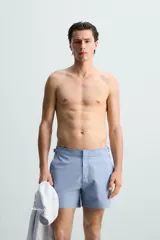 Short de baño celeste de tejido técnico con cintura elástica ajustable con cordón interior y trabillas laterales. Tiene bolsillos frontales y bolsillo trasero con cierre de cremallera. Cuenta con forro interior y cierre frontal con cremallera y botón a presión oculto.