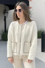 Chaqueta color crema confeccionada en lana merino hervida, con cuello redondo, cierre frontal con ganchos metálicos, bolsillos de parche y flecos en el ruedo.