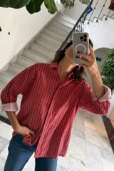 Camisa oversize a rayas verticales rojas y marrones, con cuello clásico, cierre frontal con botones y mangas largas con puños abotonados.