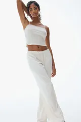 Pantalón de pijama color blanco roto, confeccionado en tejido pointelle suave. Presenta piernas levemente acampanadas, elástico revestido en la cintura con cordón fino para ajustar y ribete de volados.