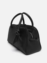 Bolso bowling de piel granulada color negro, marca Jacquemus, modelo Le Petit. Tiene cierre con cremallera bidireccional y bolsillo interior. Incluye bandolera ajustable y extraíble, y detalle de lazo decorativo en el frente.
