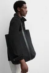 Bolso tipo shopper fabricado en piel de alta calidad con acabado serraje color negro. Tiene compartimento principal con cierre de imán, bolsillo interior con cremallera y asas de mano de piel.