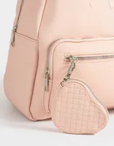 Mochila pequeña de cuerina color rosa pálido, con moño en relieve en el frente y llavero con forma de corazón trenzado. Tiene correas regulables, manija superior, cierre superior, bolsillo frontal con cierre y bolsillos laterales.