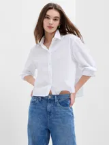 Camisa blanca de poplin, corte crop, con cuello clásico, cierre frontal con botones y mangas 3/4 con puños abotonados.