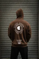 Canguro marrón con capucha, cordón ajustable y puños y cintura acanalados. Estampado en la espalda con el logo de la marca y la frase "Every rep, every drop of sweat, every early morning - It's all for the Gains. Sharpen the mindset. Own the grind".