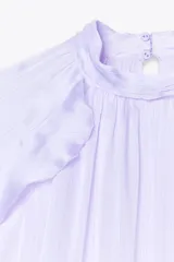 Camisa lila de cuello redondo y manga larga con volantes en el mismo tejido. Cierre en la espalda con aberturas y botones.