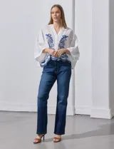 Blusa blanca con bordado floral azul, escote en V, manga japonesa y cierre frontal con botones.