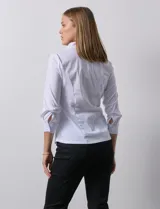 Camisa blanca de algodón con cuello a la base con solapa y escote en V. Abertura central con botones, delantera con detalles plisados y manga ¾ con puño y botón. Laterales en tejido modal.