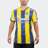Camiseta de fútbol Le Coq Sportif del Rosario Central, modelo titular temporada 25/26. Diseño a rayas verticales amarillas y azules, con un patrón geométrico sutil en las franjas azules. Presenta cuello en V y detalles en azul en mangas y hombros.