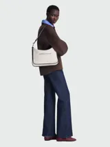 Bolso de hombro Longchamp modelo Essential Toile, tamaño L, color marfil con detalles en negro y logo de la marca estampado en el frente. Cuenta con correa de hombro ajustable y cierre superior con cremallera.