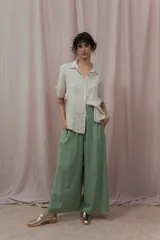 Camisa color crudo confeccionada en lino, de corte holgado, con cuello clásico, mangas cortas con dobladillo y cierre frontal con botones. Presenta detalle de pliegues verticales en la parte frontal.