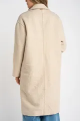 Tapado largo color beige claro, de corte oversize, con cuello solapa y cierre frontal de botones.