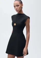 Vestido corto negro con cuello Perkins y corte peplum. Sin mangas y con cierre de botón en la parte posterior.