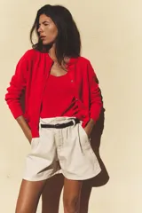 Chaqueta roja de punto con cuello redondo y manga larga. Tiene bolsillos delanteros de plastrón, cierre frontal con botones dorados con relieve y acabados en rib.