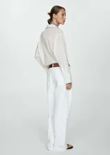 Camisa blanca de algodón con cuello camisero, manga larga con puños abotonados y cierre frontal con botones.