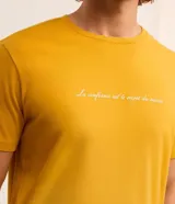 Remera de hombre color mostaza, de corte comfort, con cuello redondo y manga corta. Estampa frontal con la frase "La confiance est le secret du succès" en color blanco.